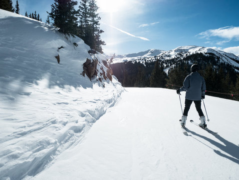 SKIER WITH NICE VIEW OF SKI TRIAL AND PINE TREES IN COLORADO IN BRIGHT BLUE SKY