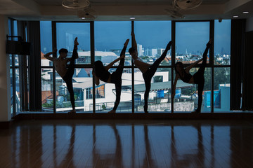 Silhouettes of four slim people standing in various dance poses while practicing in dark studio in evening