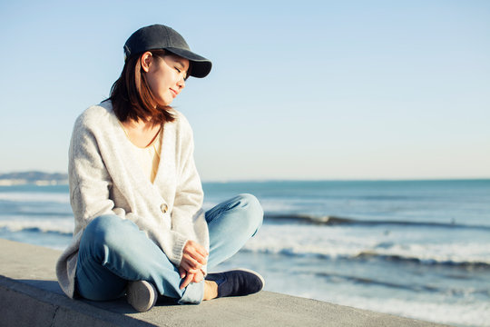 Young woman sitting on retaining wall and looking at sea