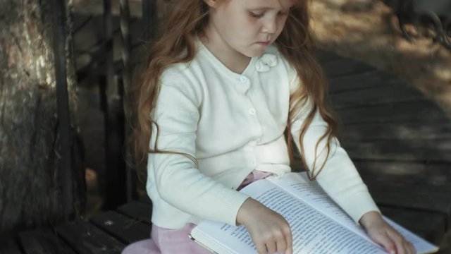 A sweet girl sits in the woods and reads a book