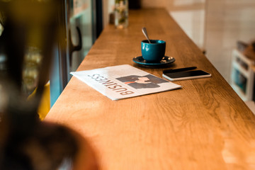 Fototapeta na wymiar smartphone, business newspaper and cup of tea on table in cafe