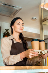 low angle view of brunette waitress holding coffee in paper cups in cafe