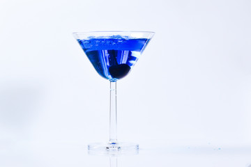Cocktail with blue liquid in glass. Glass with blue water pouring with liquid with splashes and drops. Martini glass filling with alcohol with splashes on white background. Refreshing drink concept.
