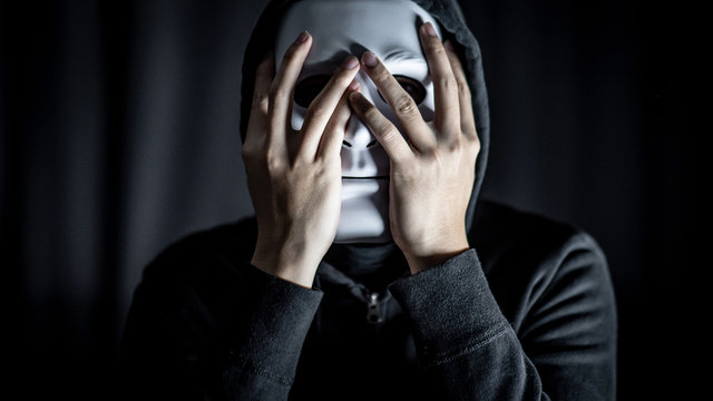 Mystery hoody man wearing white mask in the dark room. Anonymous social masking. Major depressive disorder or bipolar disorder. Halloween concept