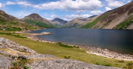 Fototapeta na wymiar Stunning landscape view of Wast Water and fells in the Lake District National Park in the UK on a beautiful sunny day. Unidentified people paddle boarding on the lake