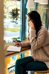 brunette female freelancer talking on smartphone and writing in diary in cafe