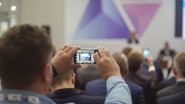 A young man takes pictures of a semenar and a business exhibition.