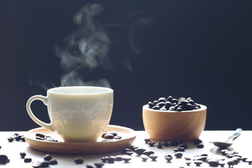 Selective focus of Coffee cup and beans with smoke rising on dark background