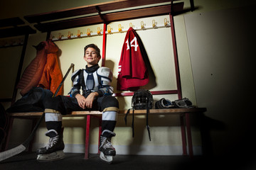 Naklejka premium Happy boy sitting in ice hockey dressing room