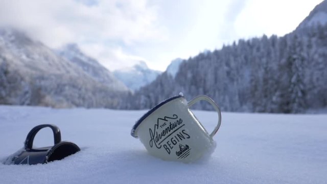 Slow motion close up of two cups with a sign adventure begins lying on a snow