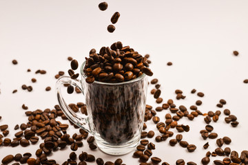Grains of coffee are poured into a glass cup on a white background