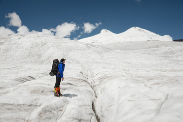 Traveler in a cap and sunglasses with a backpack on his shoulders in the snowy mountains on the...