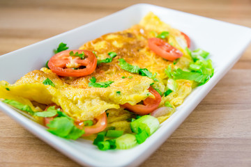 A photo of an omelette with cherry tomatoes, parsley. and grated cheese, shot from above on a rustic wooden texture with a place for text