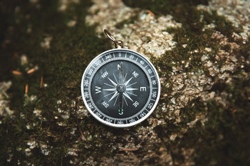 Magnetic compass with a black dial on a wild stone covered with green moss. The concept of finding the way and navigation