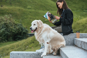 young woman reading magazine while sitting with dog in park