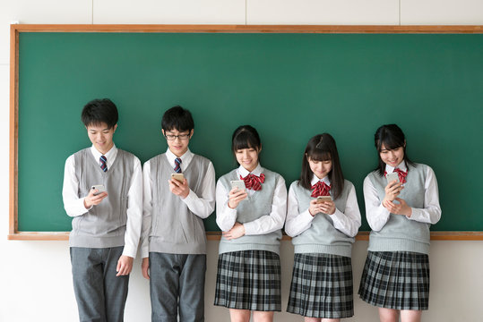 黒板の前でスマートフォンを見る学生