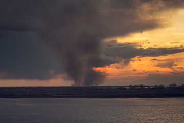 Naklejka na ściany i meble environmental pollution problem of fire on dry grass with smoke onthe horizon inflated by a strong wind during the sunset