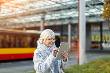 Senior woman using tablet, while waiting for the bus
