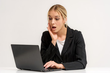 Studio photo of a beautiful blonde girl is talking on a white background sitting at a table with a laptop.