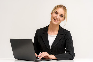 Studio photo of a beautiful blonde girl is talking on a white background sitting at a table with a laptop.