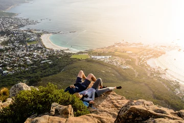 Washable wall murals Camps Bay Beach, Cape Town, South Africa A couple is relaxing on top of Lion's Head mountain in Cape Town and enjoying the beautiful sunset with a view of Camps Bay and Clifton Beach areas