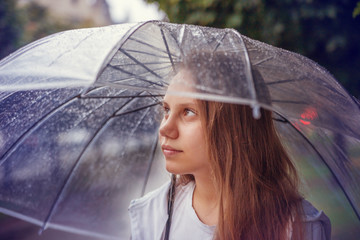School-age girl under a transparent umbrella in the rain.