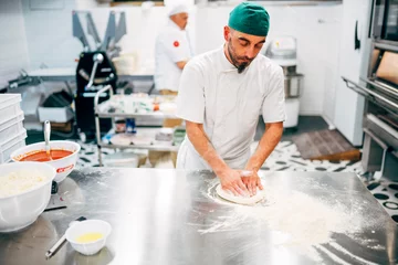 Fotobehang Man works in the restaurant making pizza at the pizzeria. © OscarStock