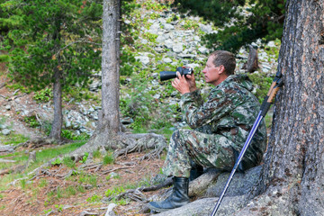 The tourist looks through the binoculars to the mountains. A man looks in a telescope to the top of the mountain.