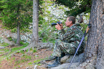 Naklejka premium The tourist looks through the binoculars to the mountains. A man looks in a telescope to the top of the mountain.