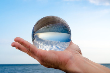man's hand holds a glass orb lens in which an inverted reflectio