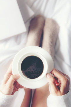Close up legs women on white bed. Women reading book and drinking coffee in morning relax mood in winter season. Lifestyle Concept..