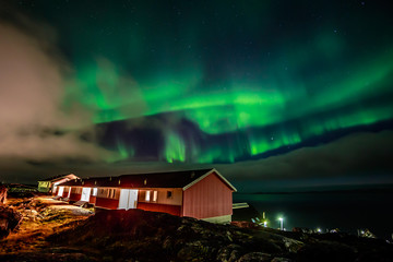 Green bright northern lights hidden by the clouds over living houses at the fjord, Nuuk city,...