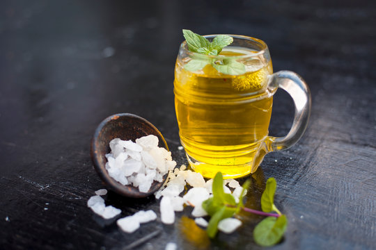 Close up of refreshing mint and lemon cooler in a transparent glass on wooden surface with raw lemon and juice and sugar.