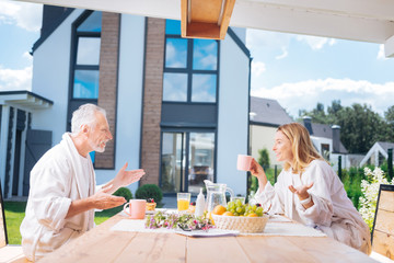 Emotional conversation. Happy beaming couple feeling cheerful while having emotional conversation while eating their breakfast