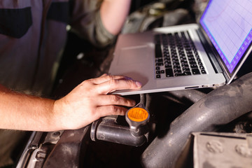 Closeup hands of mechanic with the help of diagnostic machines is ready for use with the car. Laptop torque figures and horsepower is the engine of the vehicle for diagnostics and configuration.