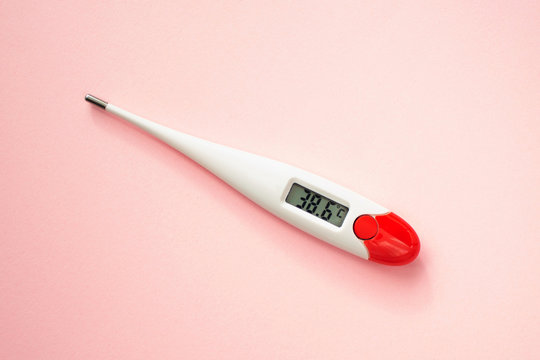 White digital clinical thermometer on pink background shows fever heat temperature