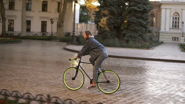 Woman riding bike on city paved road. Woman bicycle rider have a ride in the morning. Empty city street with a beautiful old buidings on the background. Side view