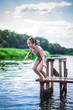 Little cute girl jumping off the dock into a beautiful river at sunset