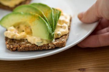 Frau isst Avocado Eiersalat Brot mit Vollkorn Sonnenblumenkern und Kurkuma zum Frühstück