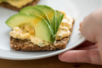 Frau isst Avocado Eiersalat Brot mit Vollkorn Sonnenblumenkern und Kurkuma zum Frühstück