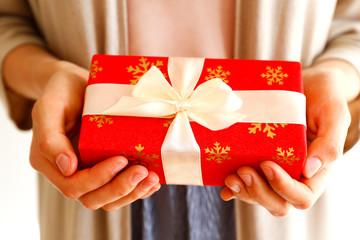 Young casual woman wearing pink shirt and long beige cardigan holding a beautiful present in shiny wrapping tied with golden bow. Giftwrapping concept. Background, copy space, close up.