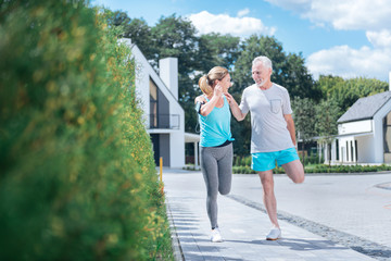 Fototapeta na wymiar Stretching after jogging. Happy mature couple feeling amazing while stretching after jogging near their house together