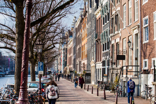 People walking and riding bicycles at the beautiful cobblestone streets next to the canals of the Old Central district of Amsterdam