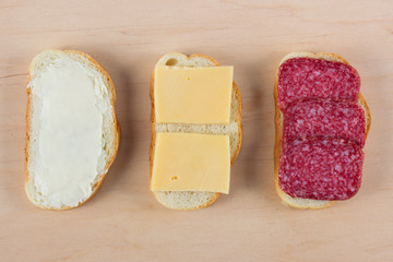 bread slice with butter, with cheese, with salami, on a wooden background, Set of simple sandwiches, top view, flat lay