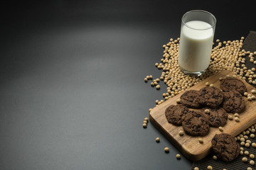 the chocolate chip cookies on the wooden tray, a glass of soy milk, a pile of soybeans and the napery on black table