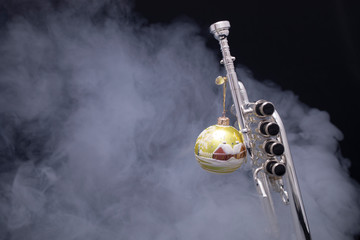 A silver plated piccolo trumpet with a christmas ornament in smoke on a black background