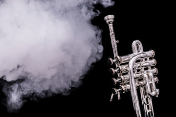 A silver plated piccolo trumpet in smoke on a black background