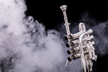 A silver plated piccolo trumpet in smoke on a black background - obrazy, fototapety, plakaty
