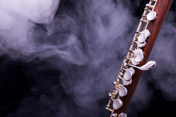 A piccolo flute from brown wood with silve plated keys in smoke on a black background