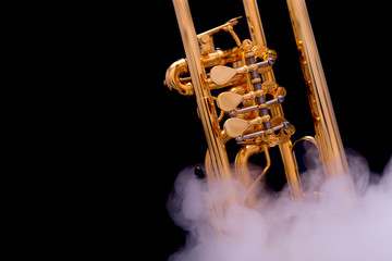 A gold plated rotary trumpet in smoke on a black background